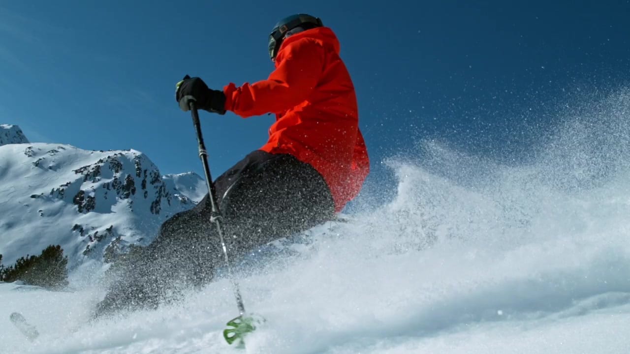 Skier in red jacket descending snowy mountain slope with fresh powder spray